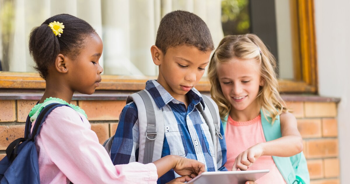 Young children standing together watching content on tablet